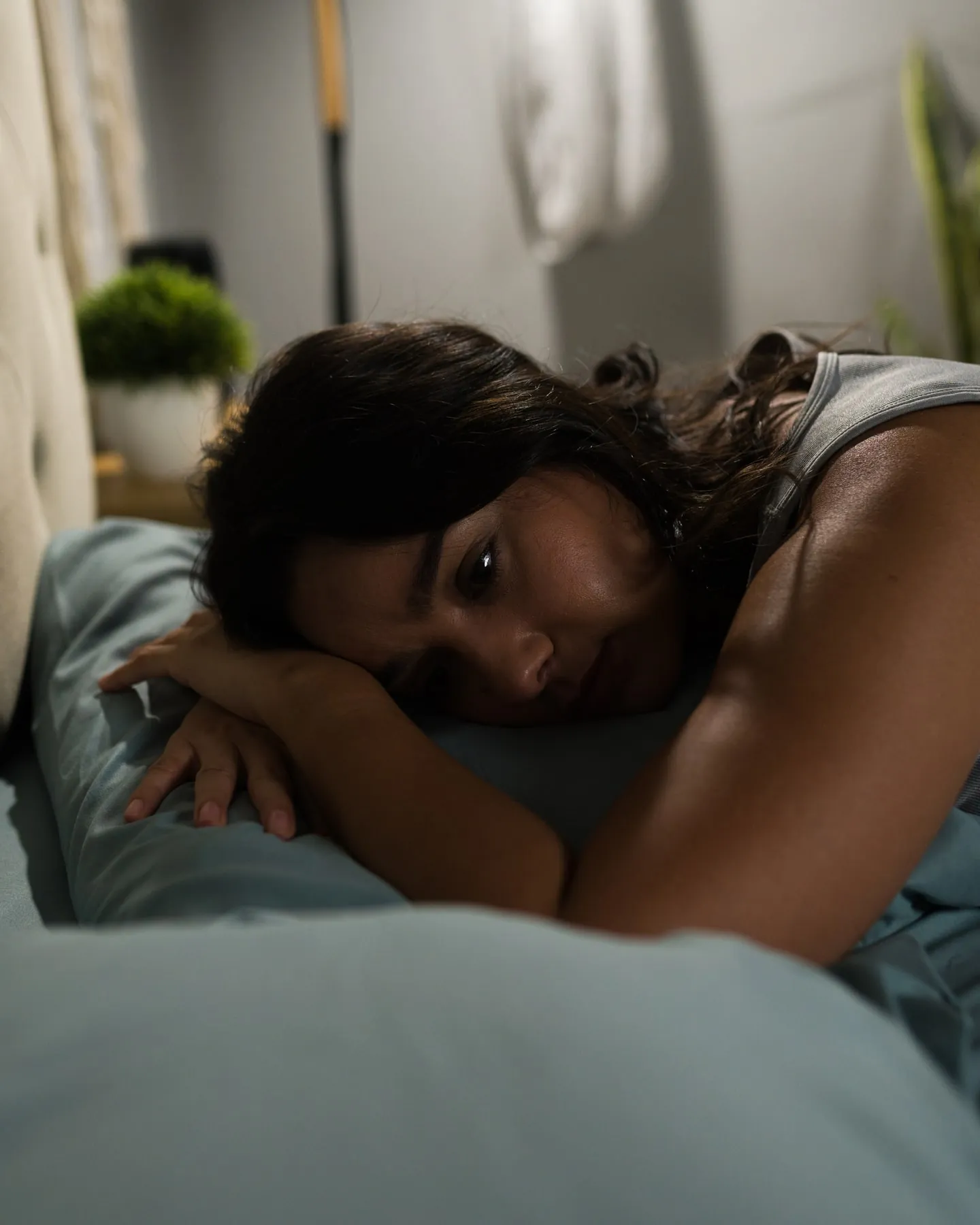A woman lies awake in bed at night, her head on the pillow and her eyes open.